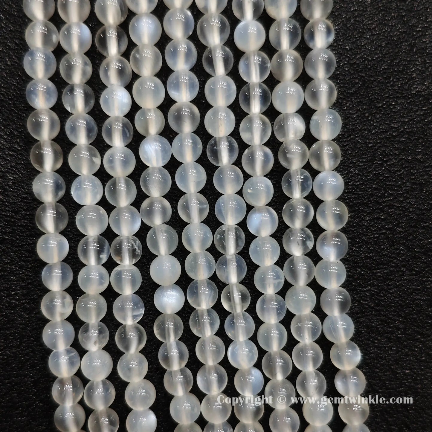 Perspective view of creamy white blue flash moonstone round beads displaying polished 5mm finish