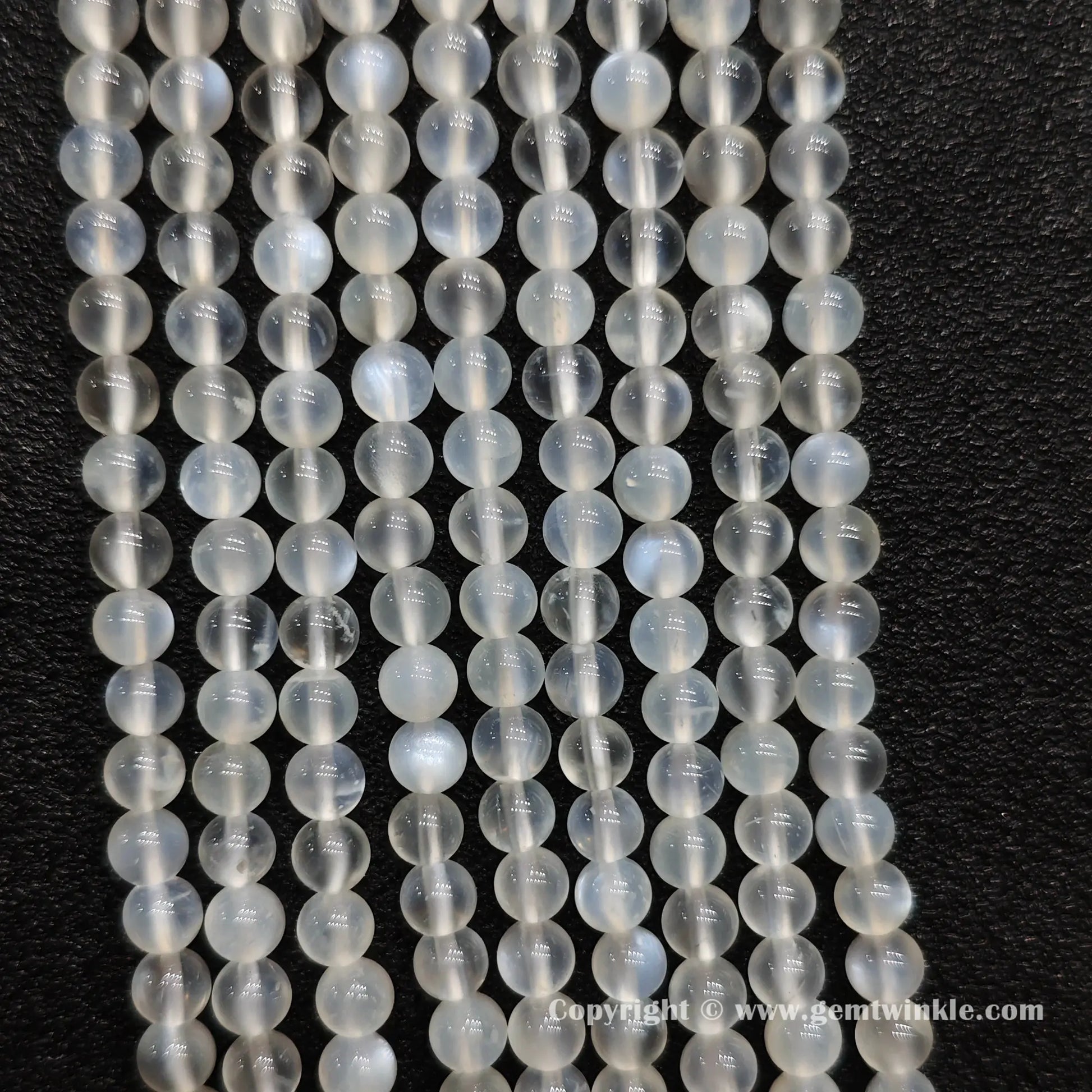 Perspective view of creamy white blue flash moonstone round beads displaying polished 5mm finish