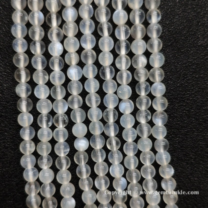 Perspective view of creamy white blue flash moonstone round beads displaying polished 5mm finish