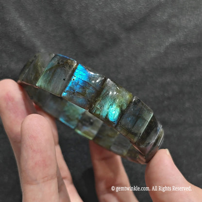 Side view of a blue flash labradorite bar cut bangle showcasing vibrant iridescent sheen across plate beads