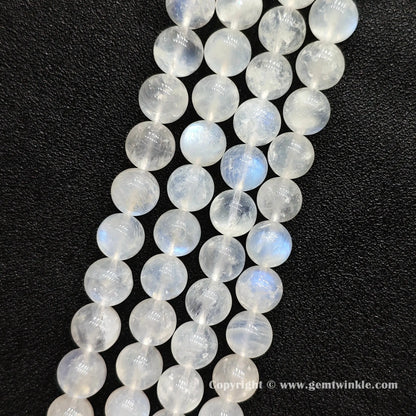Close up view of ice fractured blue flash moonstone round beads held on fingers for natural optical preview