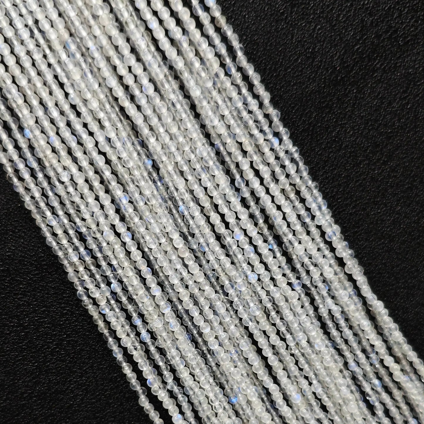 Macro closeup of 2mm blue flash moonstone smooth round seed beads showing vibrant optical blue sheen