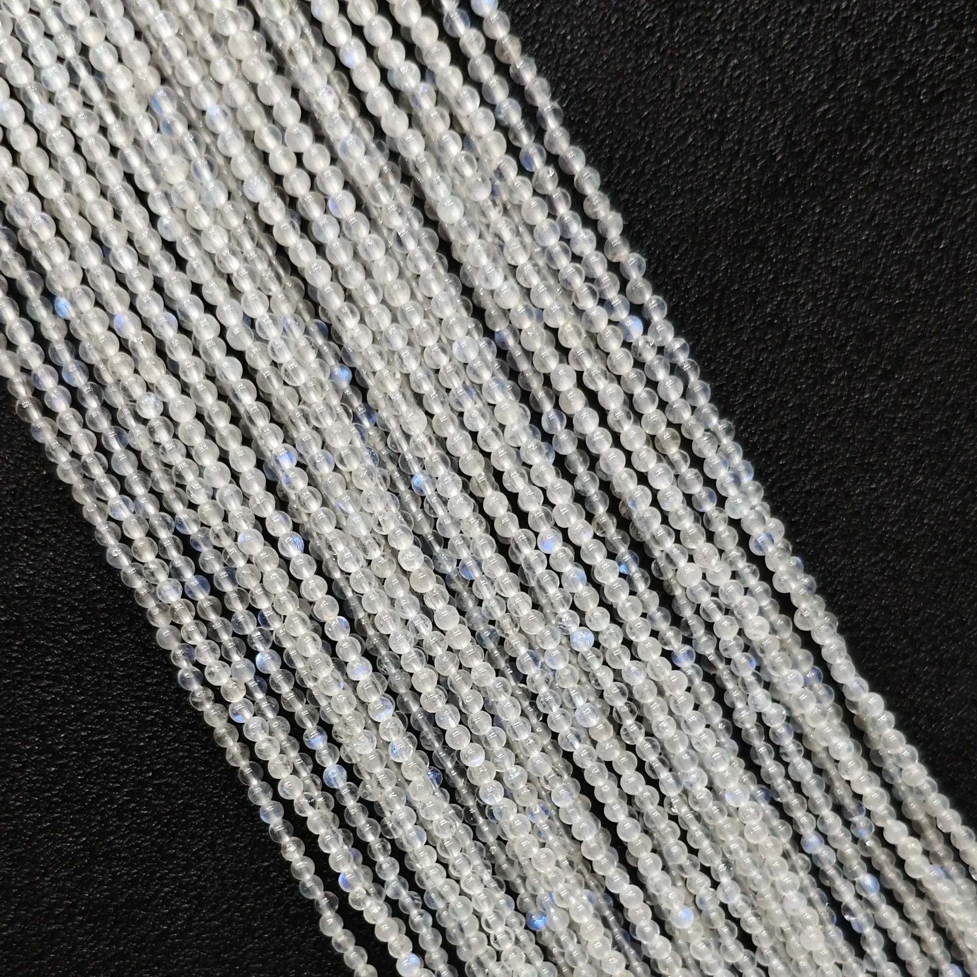Macro closeup of 2mm blue flash moonstone smooth round seed beads showing vibrant optical blue sheen