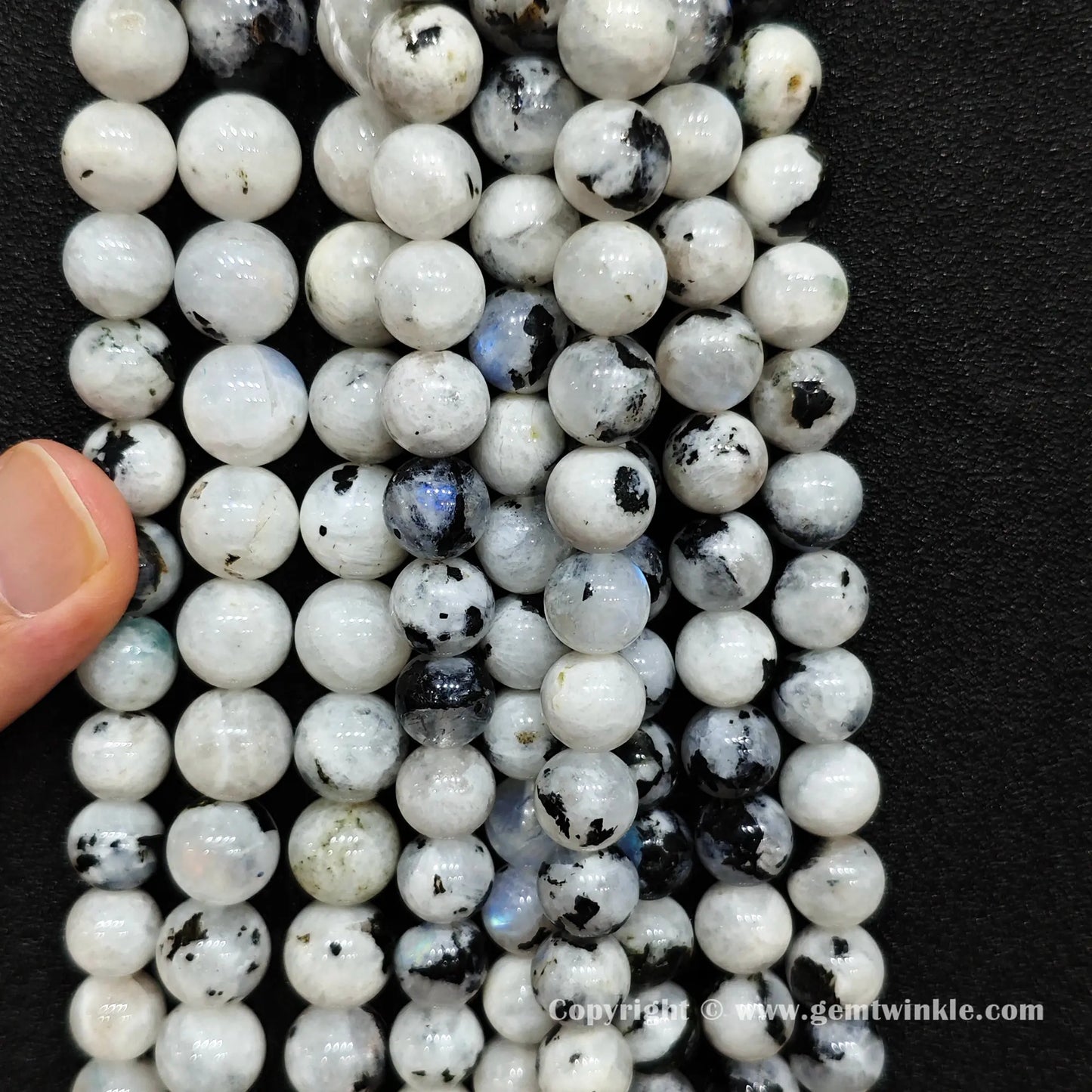 Perspective view of blue flash moonstone round beads with natural black inclusions across multiple sizes