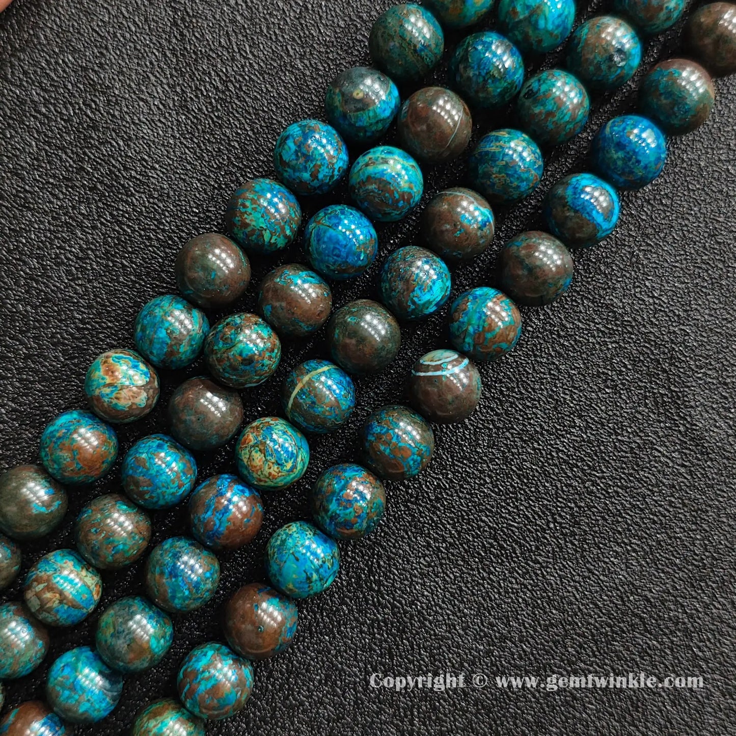 Angled view of blue phoenix stone round bead strands laid parallel on dark textured surface