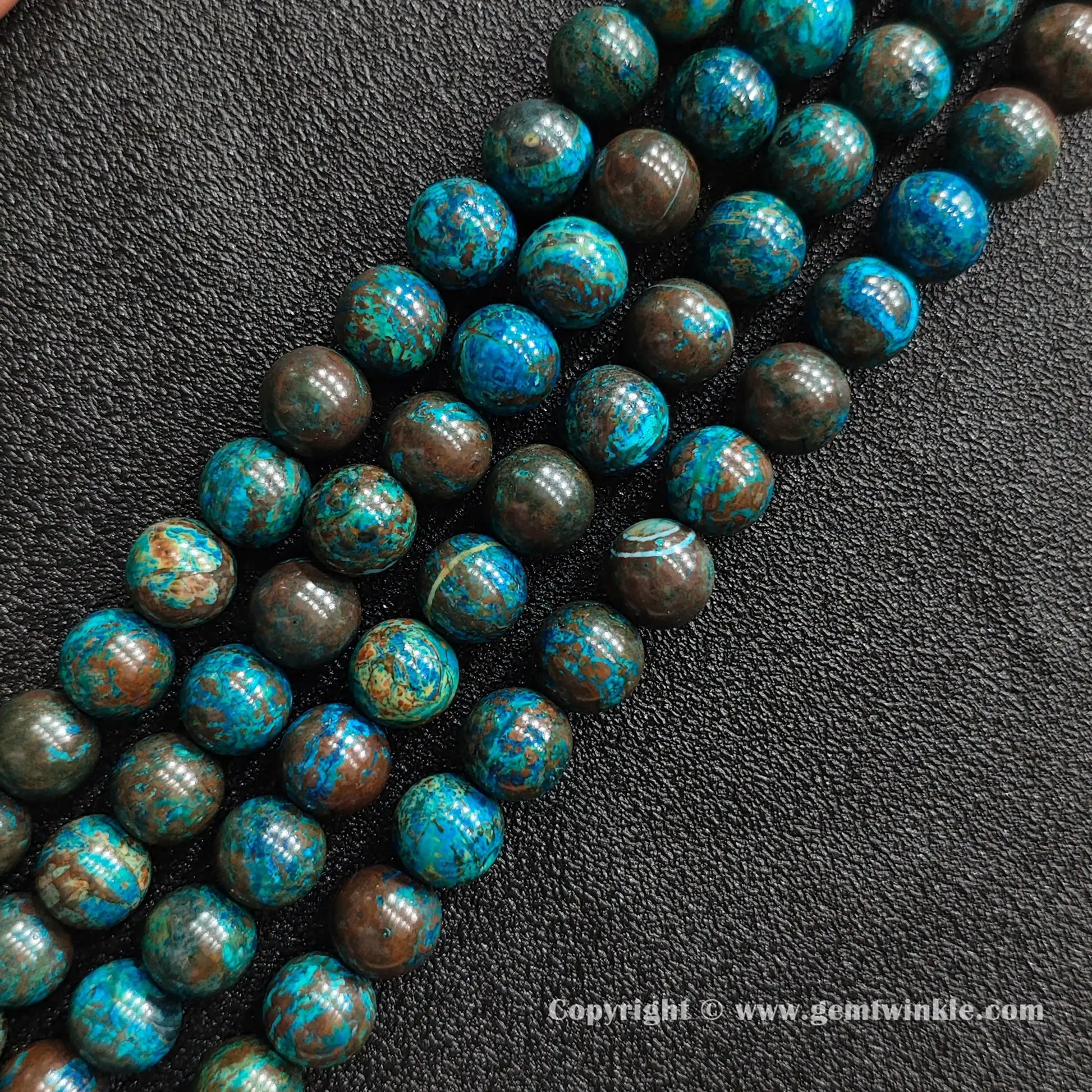 Angled view of blue phoenix stone round bead strands laid parallel on dark textured surface