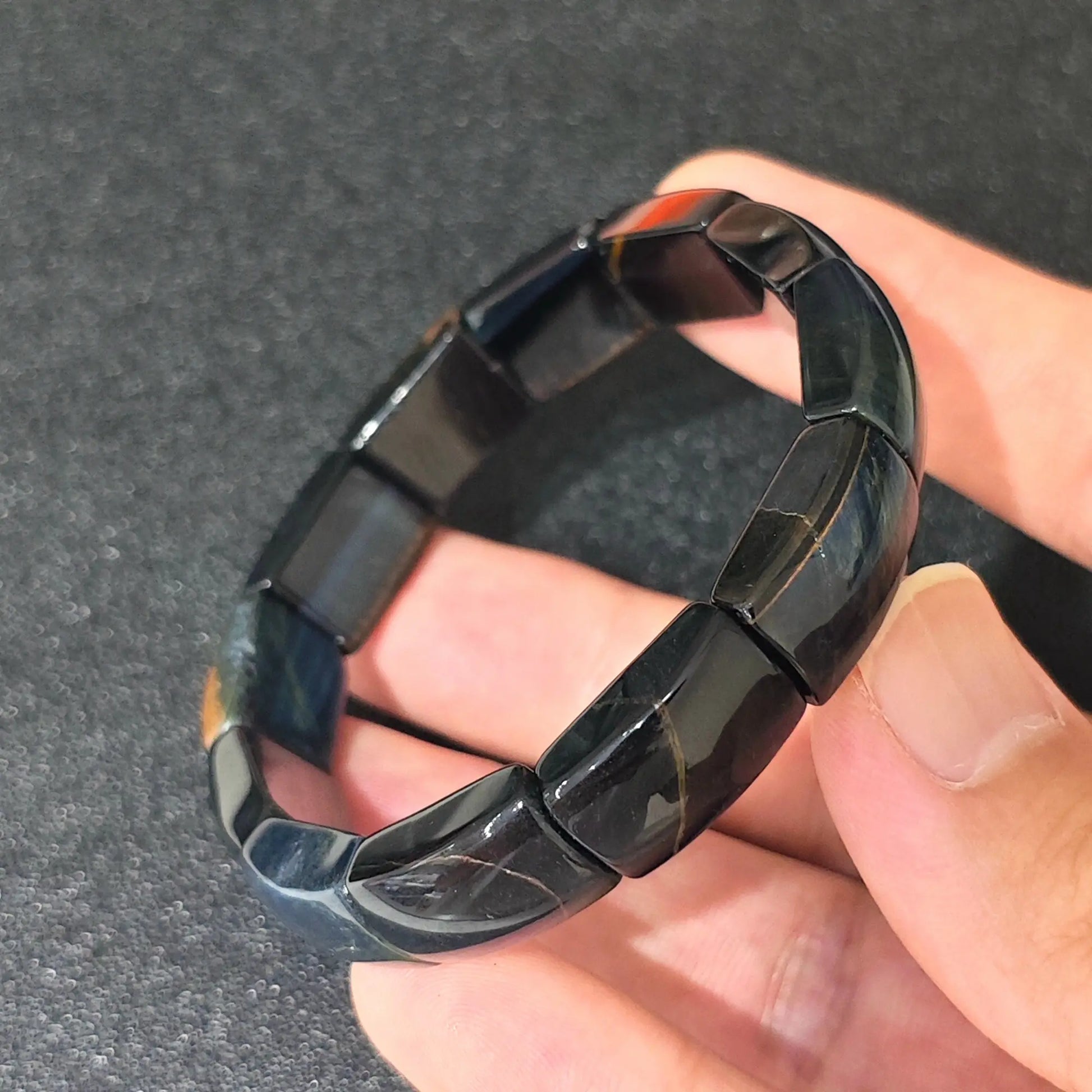 blue tigers eye curved plate bracelet resting on fingers showing silky dark blue sheen and elastic cord