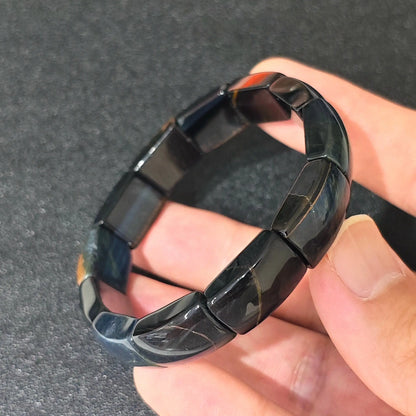 blue tigers eye curved plate bracelet resting on fingers showing silky dark blue sheen and elastic cord