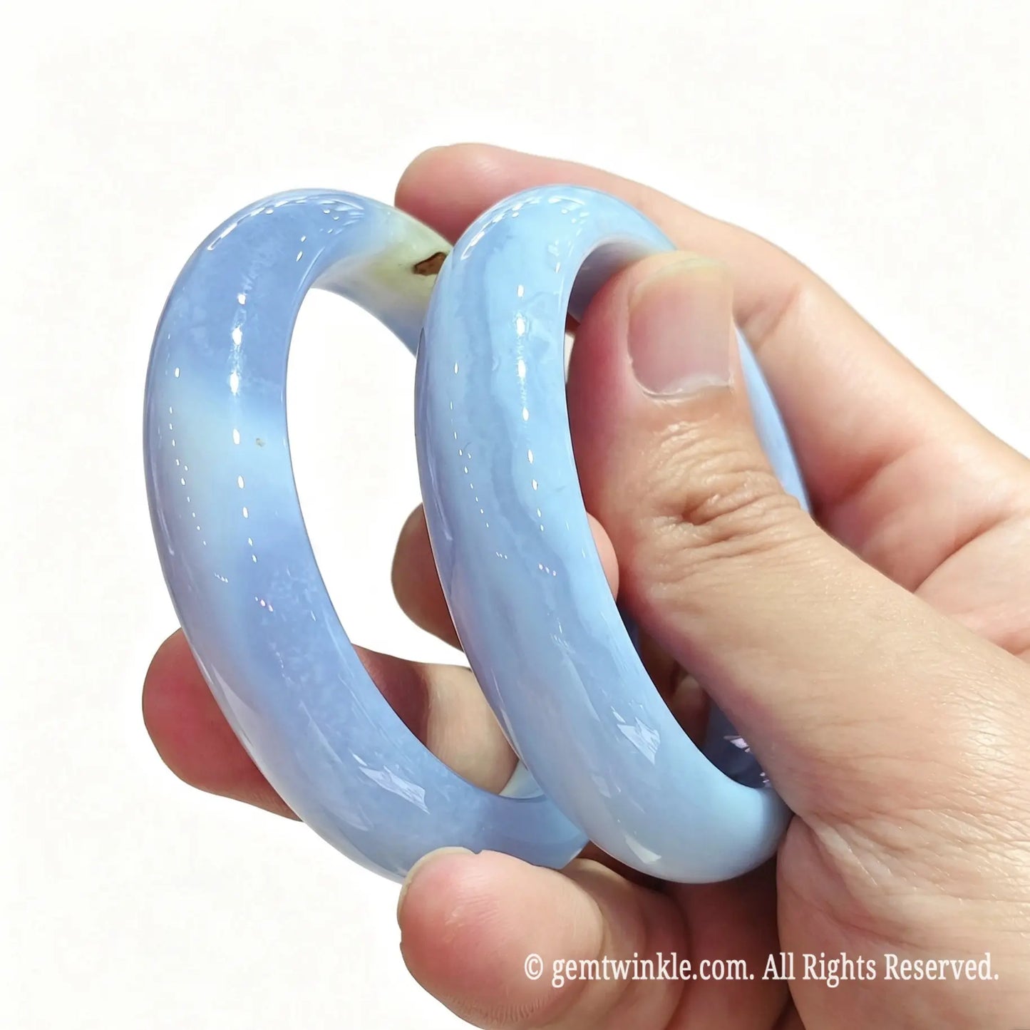 Side view of stacked blue lace agate solid bangles held between fingers showing delicate blue banding and polished finish