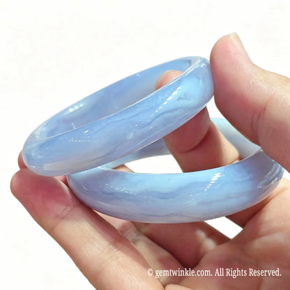Pair of smooth round blue lace agate gemstone bangles held in hand showing delicate light blue lace pattern