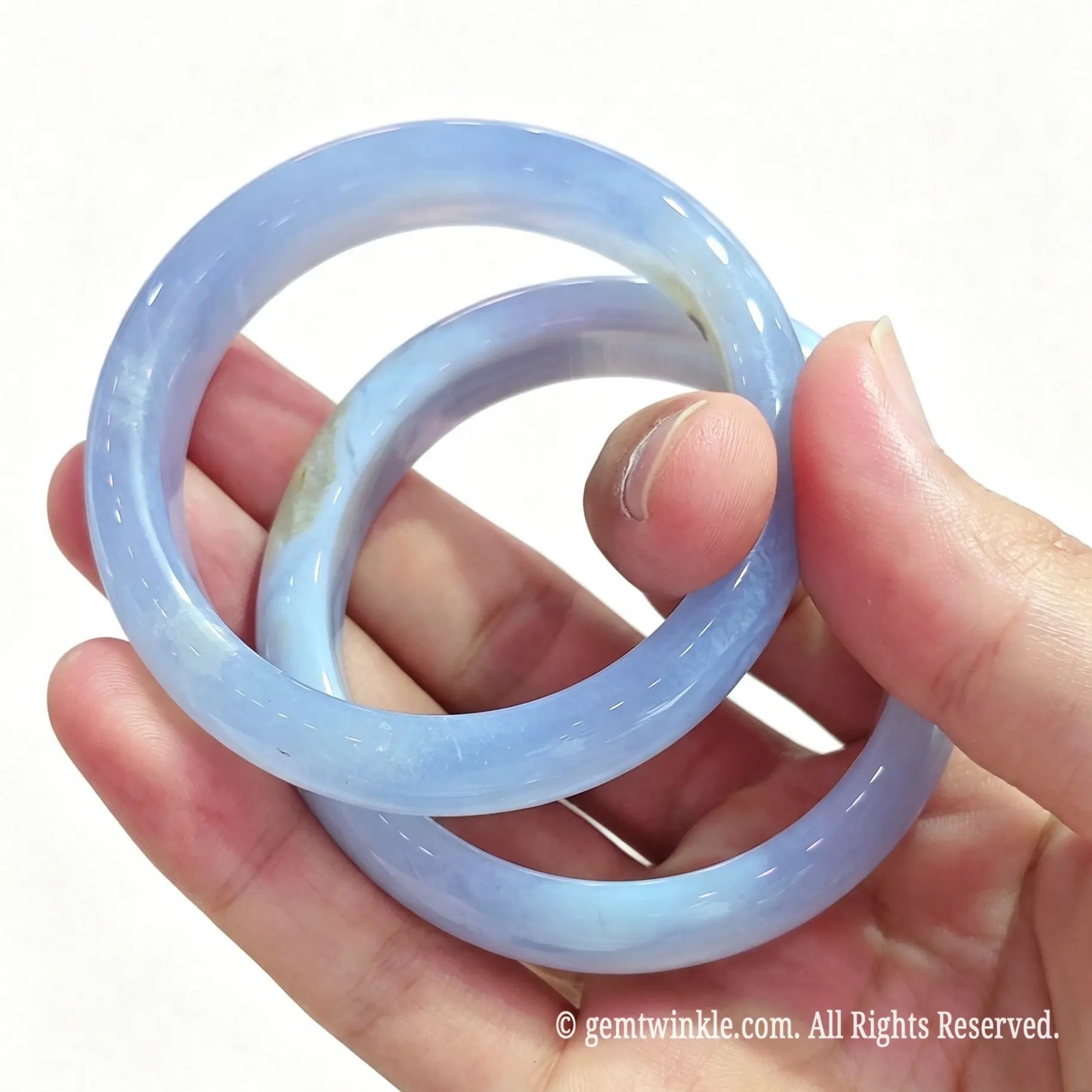 Angled hand view of two solid blue lace agate bangles showcasing smooth inner contour and natural translucent texture