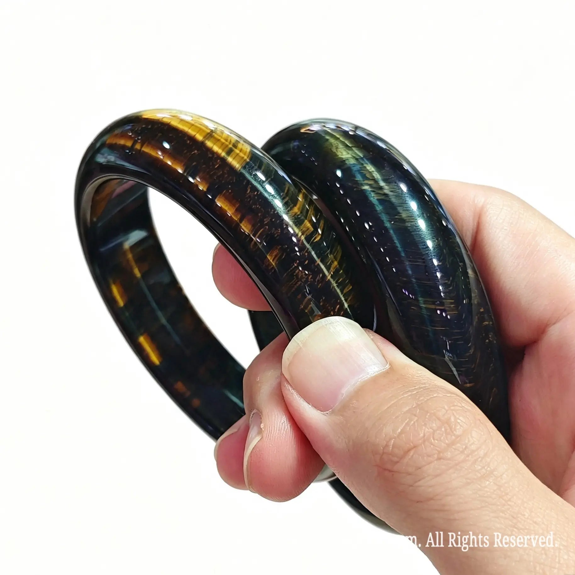Pair of stabilized blue hawk eye bangles held on fingers showing golden flash and silky mineral luster