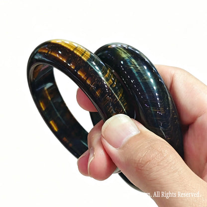 Pair of stabilized blue hawk eye bangles held on fingers showing golden flash and silky mineral luster