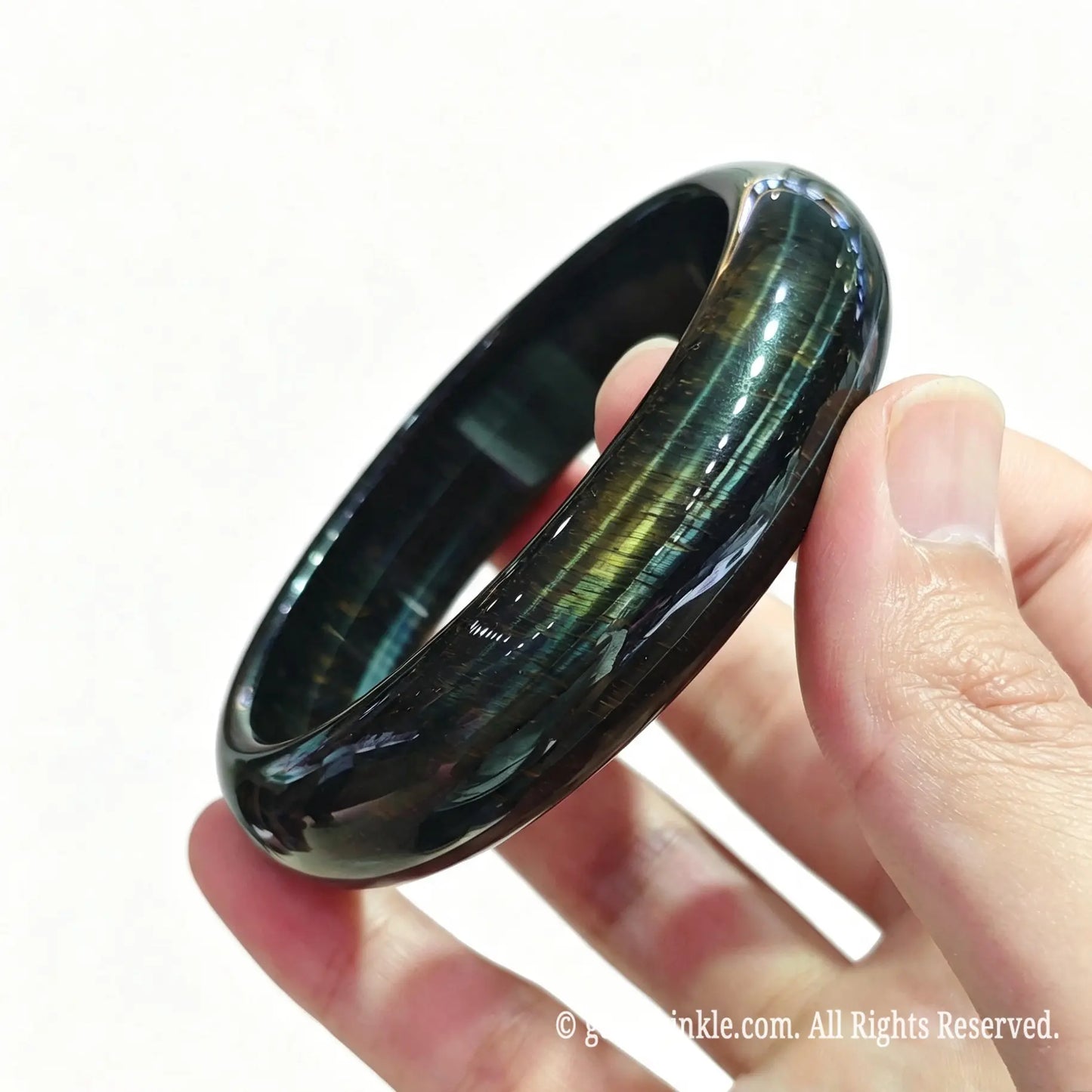 Angled hand view of a solid blue tiger eye crystal bangle showing deep ocean blue color and smooth inner contour