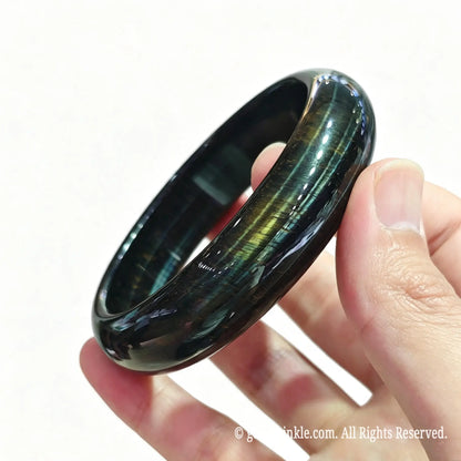 Angled hand view of a solid blue tiger eye crystal bangle showing deep ocean blue color and smooth inner contour