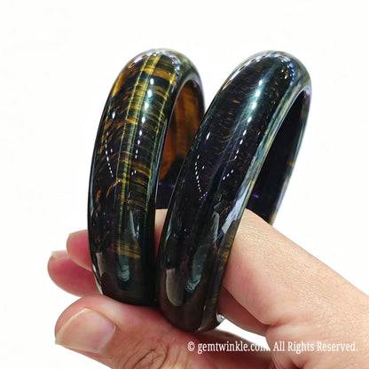 Side view of two solid blue tiger eye crystal bangles held in hand showcasing rich dark blue texture