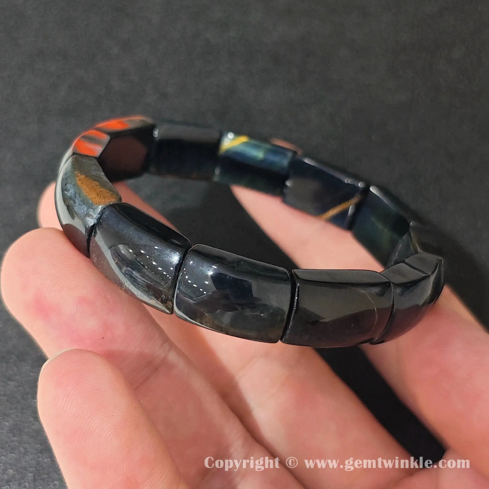 side profile view of machine polished blue tigers eye cuff bracelet held over hand