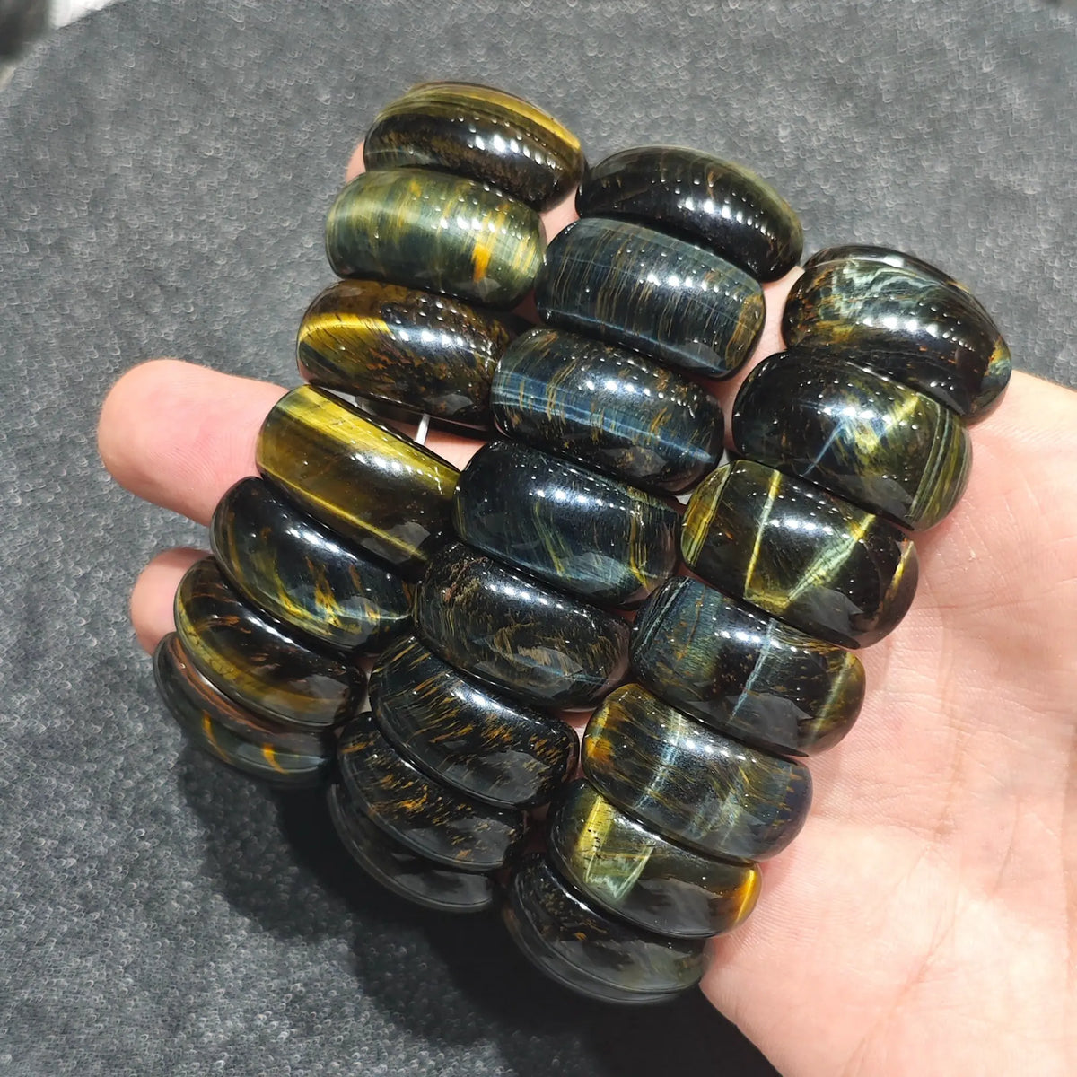 three blue and yellow tiger eye drum bead stretch bracelets resting across back of hand under direct studio light