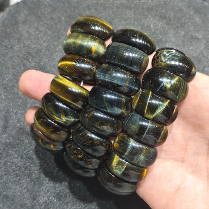 three blue and yellow tiger eye drum bead stretch bracelets resting across back of hand under direct studio light