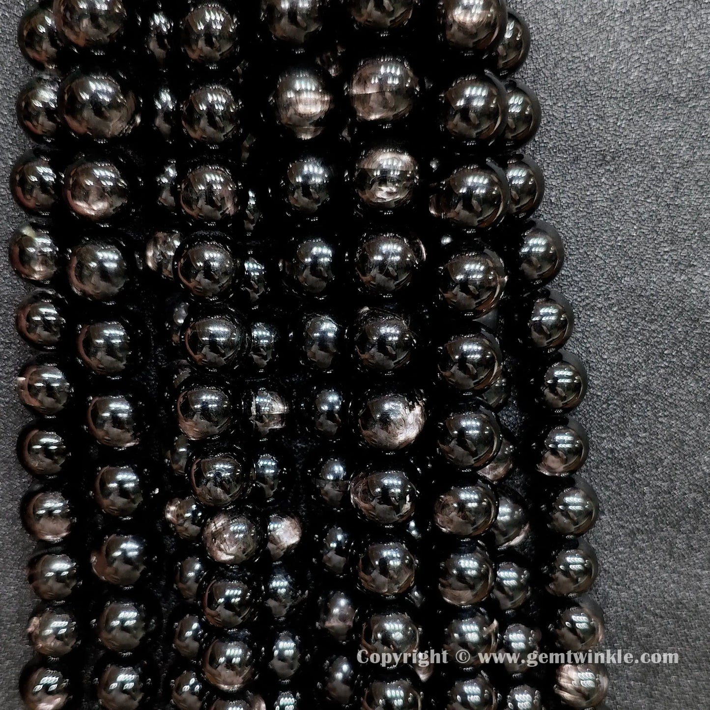 Multiple strands of B grade commercial hypersthene beads hung together showing raw earth-mined textures and natural indentations without cosmetic surface filling