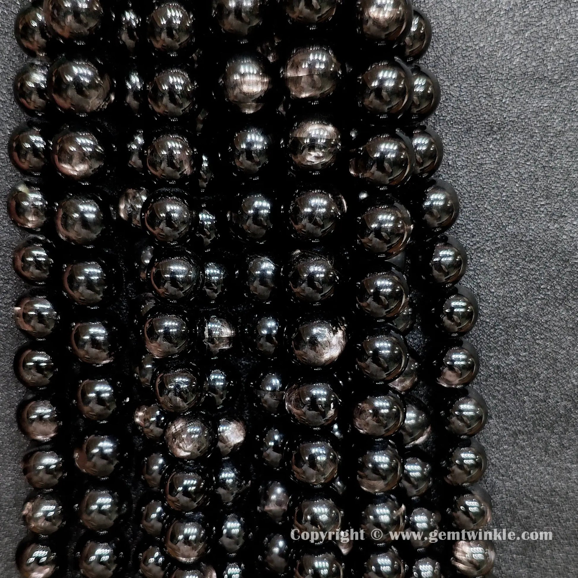 Multiple strands of B grade commercial hypersthene beads hung together showing raw earth-mined textures and natural indentations without cosmetic surface filling