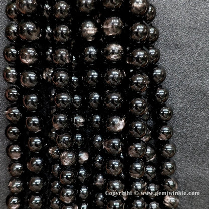 Multiple strands of B grade commercial hypersthene beads hung together showing raw earth-mined textures and natural indentations without cosmetic surface filling