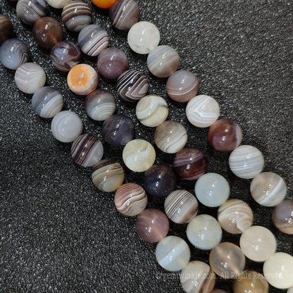 Close up view of natural un dyed banded agate strands showing beautiful concentric ribbons and earthy grey purple layers for handmade bracelet design