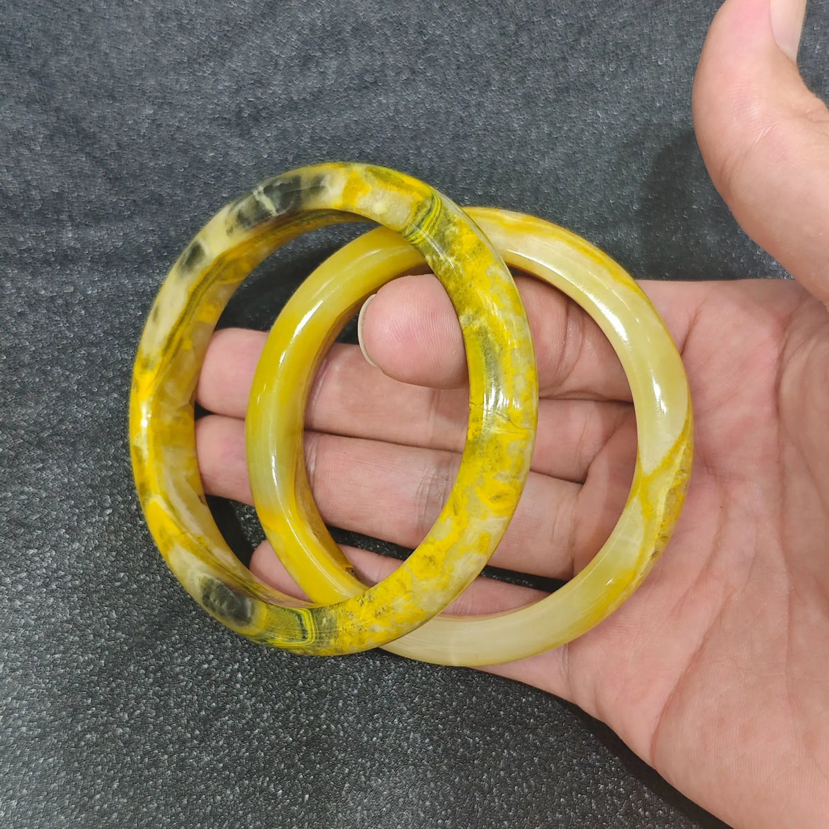 Natural Bumblebee Jasper solid gemstone bangle bracelets showing yellow and black volcanic patterns held on hand
