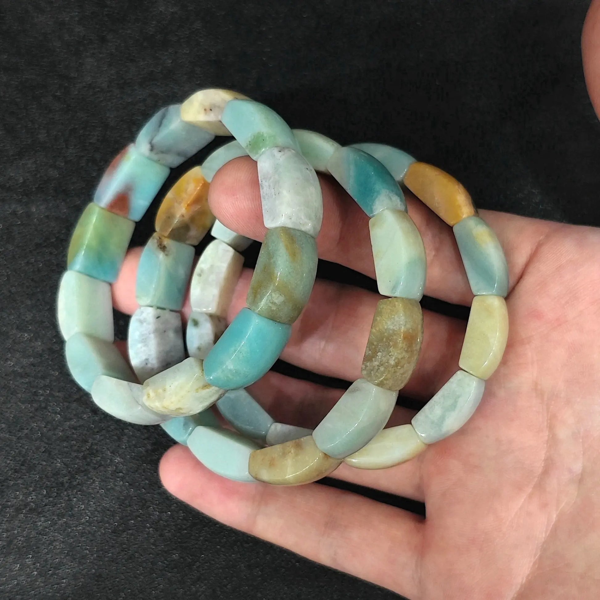 Top angle view of three circular Caribbean Calcite barrel bead stretch bracelets held in hand showing natural aragonite banding