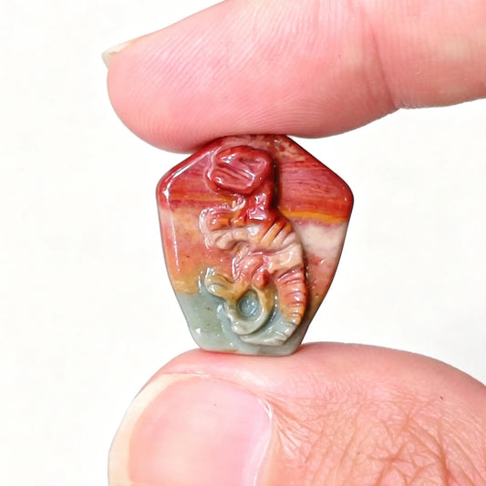 Fingers holding a hand-carved Alashan Gobi agate T-Rex dinosaur fossil skeleton relief displaying red and green earth bands