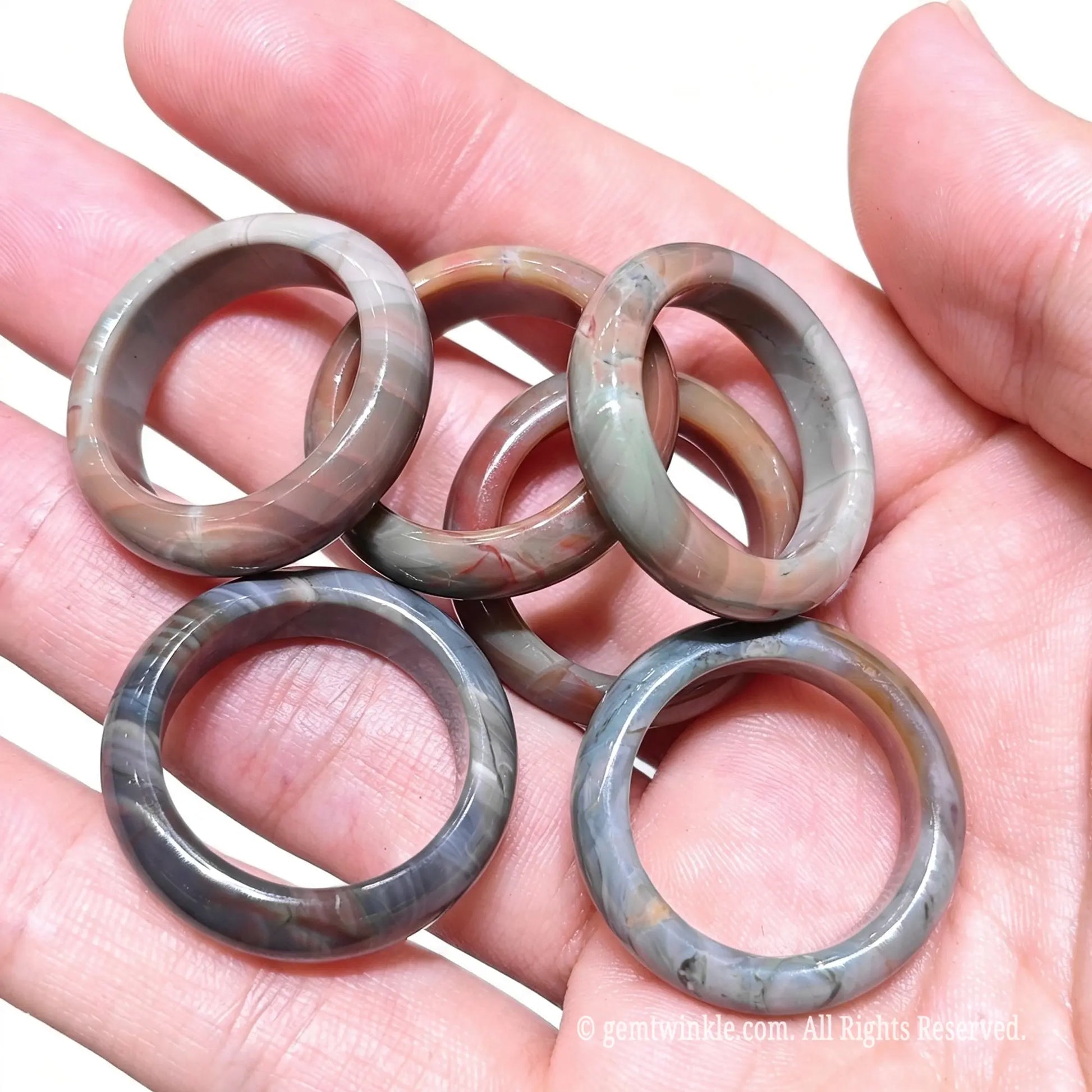 Top view of several carved Alashan desert agate finger rings resting in open palm showcasing unique earthy patterns
