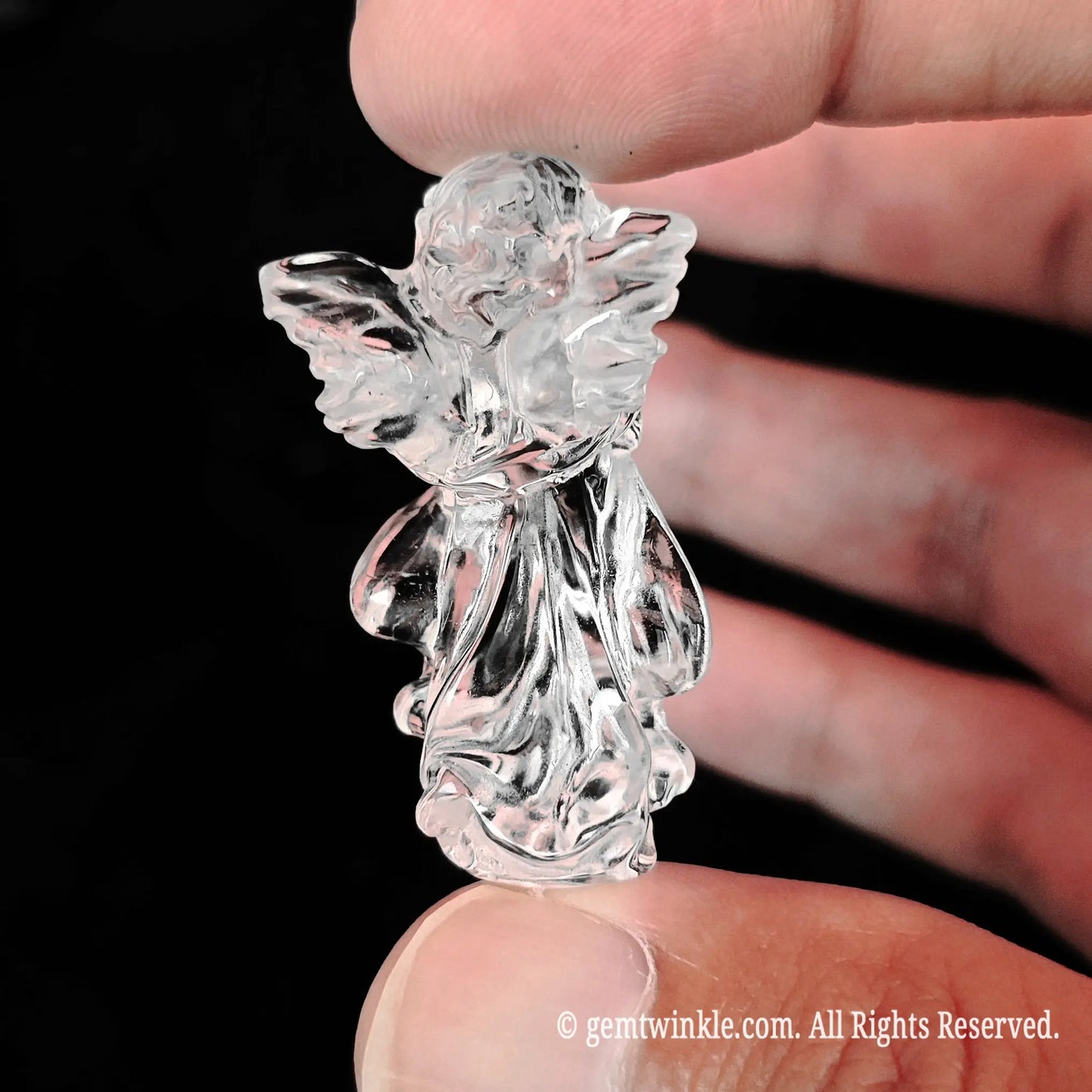Back view of hand-carved clear quartz praying guardian angel figurine held in fingers showcasing carved wing textures