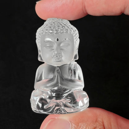 Fingers holding a 50mm transparent clear quartz carved seated buddha figurine with frosted head detail