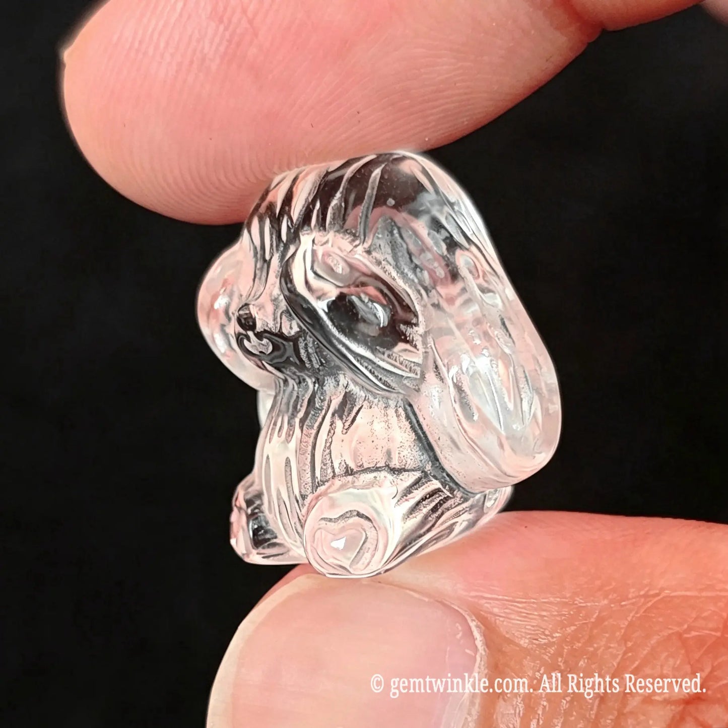 Back view of 2.5cm carved clear quartz rabbit statue held in fingers showcasing smooth polished back contours
