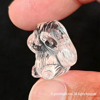 Back view of 2.5cm carved clear quartz rabbit statue held in fingers showcasing smooth polished back contours