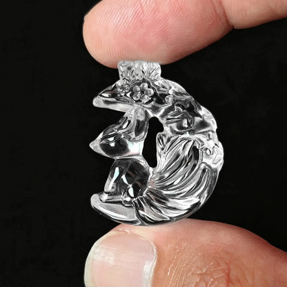 Fingers holding a 30mm transparent clear quartz carved fox resting on crescent moon pendant