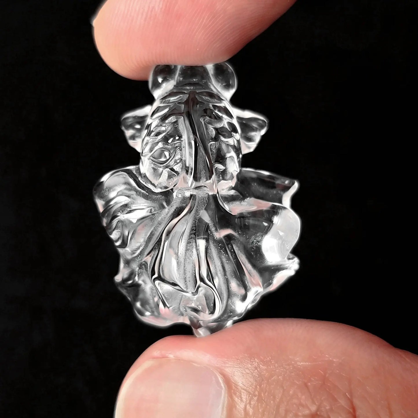 Fingers holding a 30mm transparent clear quartz carved goldfish figurine with broad flowing tail fins