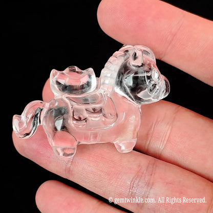 Side angle display of 5cm carved clear quartz horse figurine resting between fingertips showing smooth polished contours
