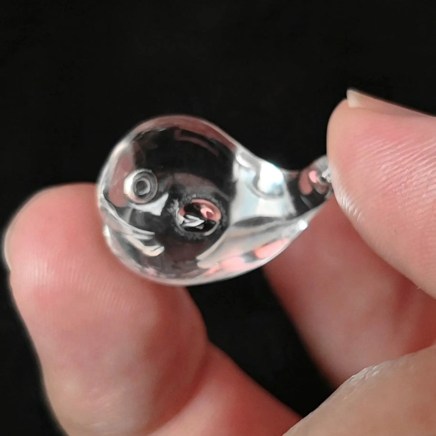 Fingers holding a 20mm transparent clear quartz carved mini whale figurine with subtle natural inclusions