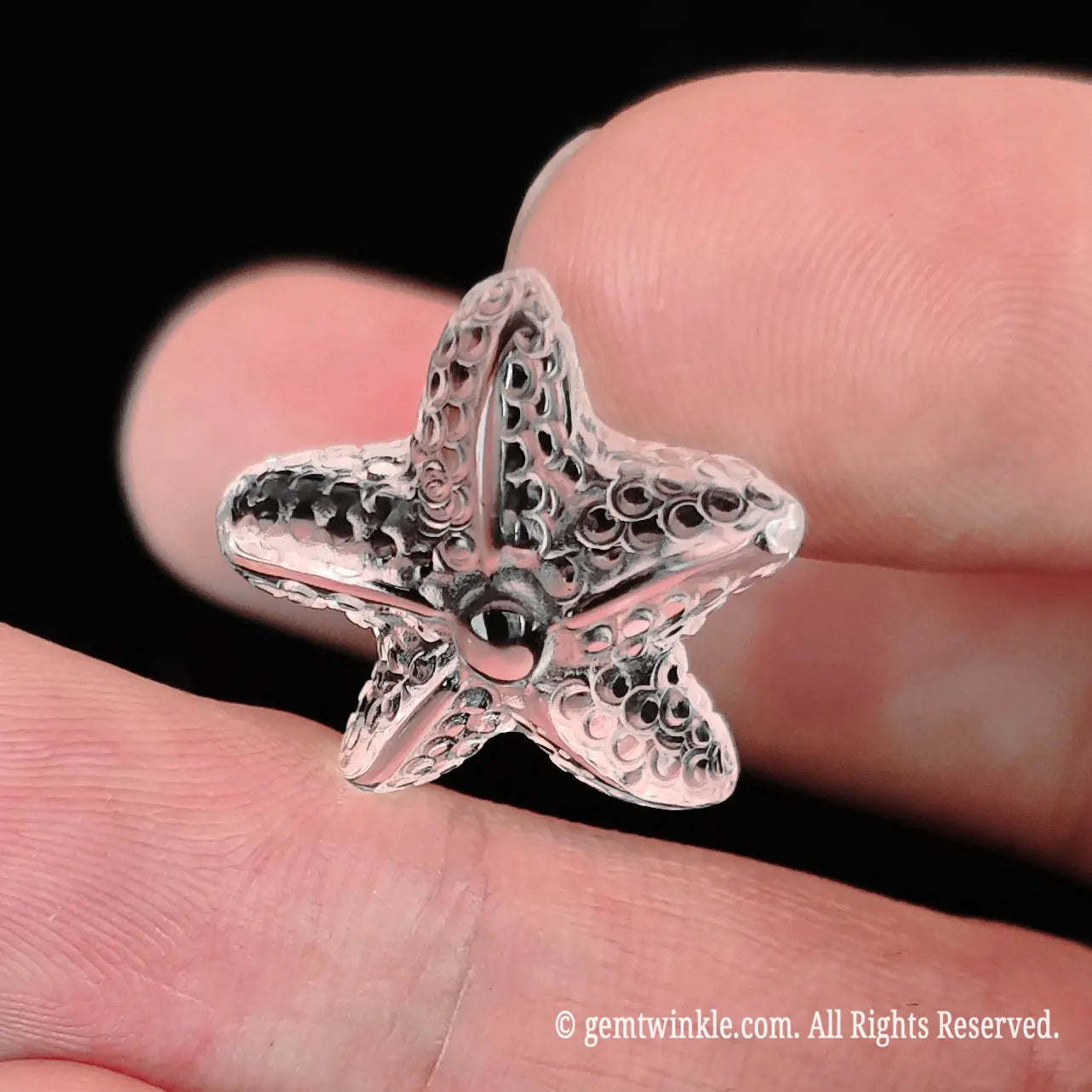 Side view of mini clear quartz starfish gemstone held between fingertips demonstrating smooth carved contours