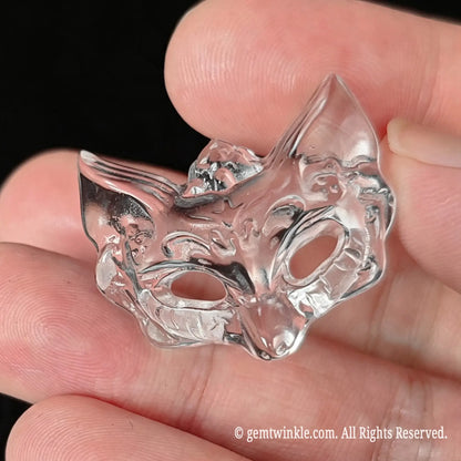 Back view of carved clear quartz fox mask pendant held between fingers showing smooth polish and crystal clarity