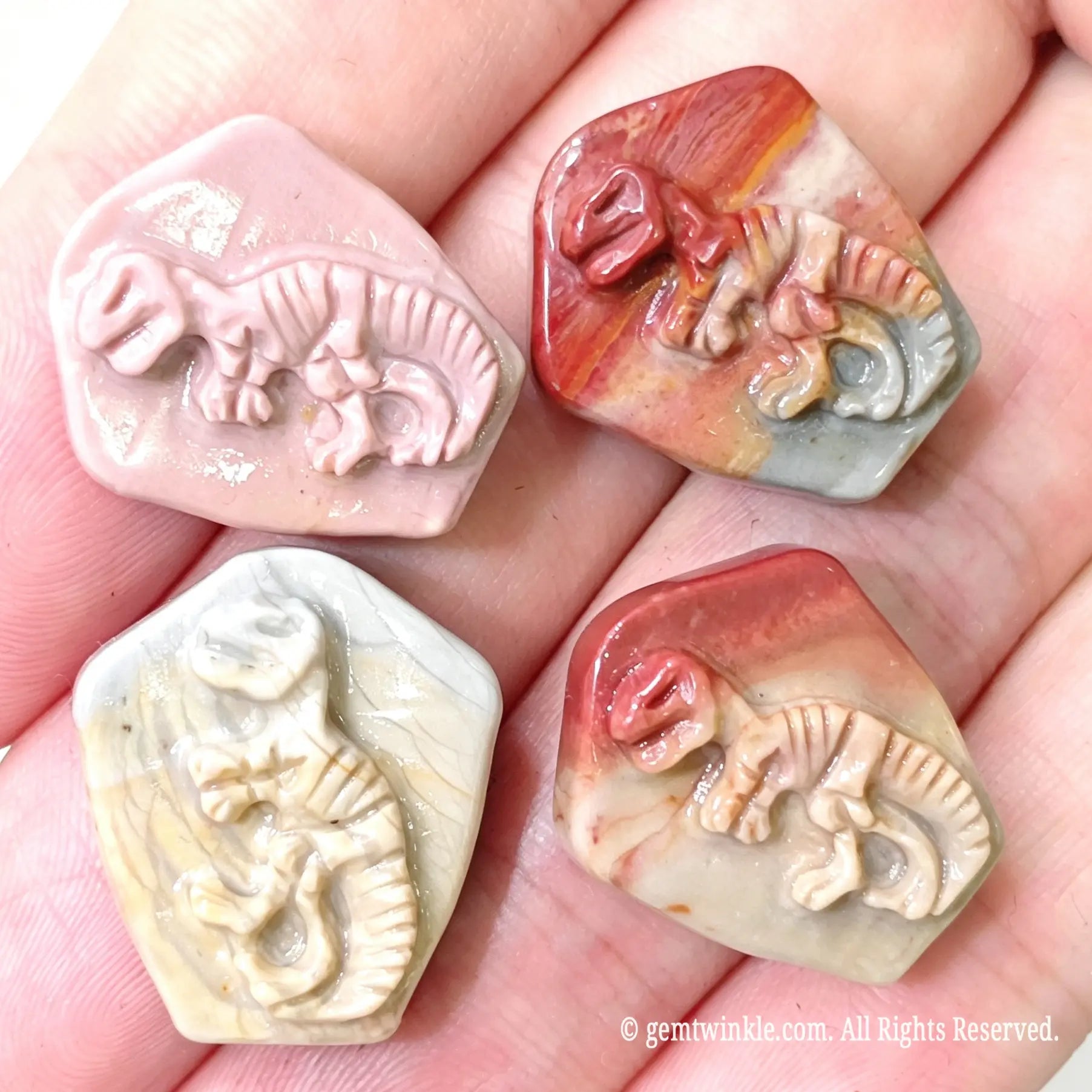 Hand holding four hand-carved Alashan agate dinosaur fossil relief cabochons showcasing detailed skeleton carvings