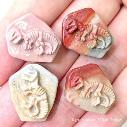 Hand holding four hand-carved Alashan agate dinosaur fossil relief cabochons showcasing detailed skeleton carvings