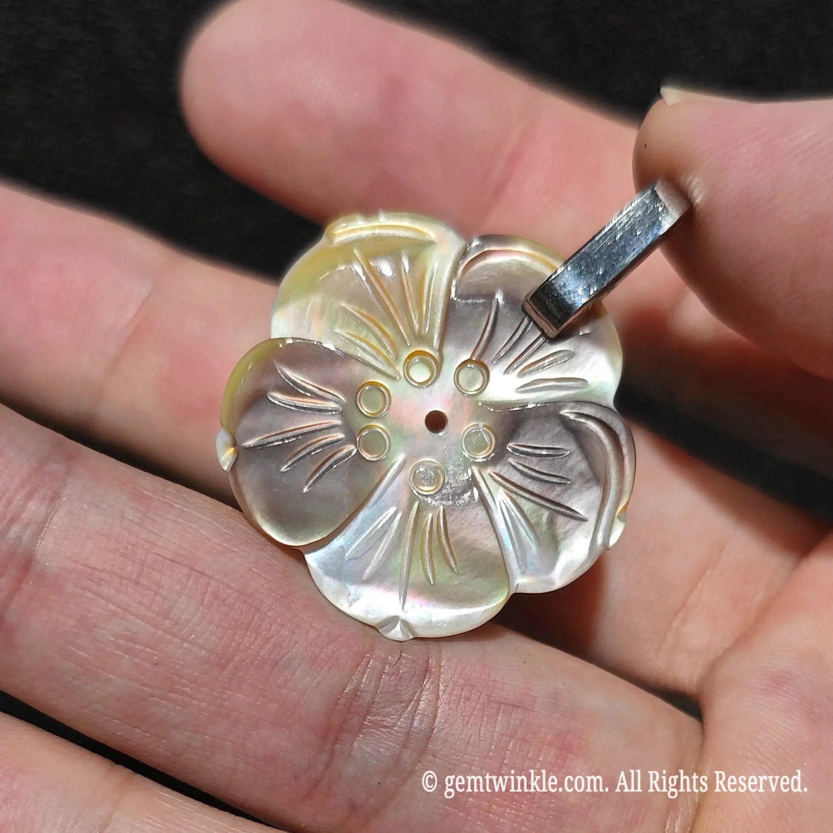 Close up view of carved grey mother of pearl flower pendant showing subtle rainbow iridescence and detailed petal relief