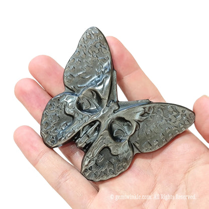 Angled view of carved silver sheen obsidian skull butterfly statue highlighting 3D carving depth and metallic shimmer