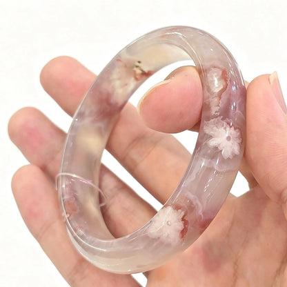 Main view of cherry blossom agate bangle held across hand showing distinct white blooming flower inclusions and icy body