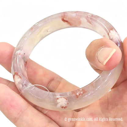 Full circular view of cherry blossom agate bangle held between fingers displaying complete floral distribution