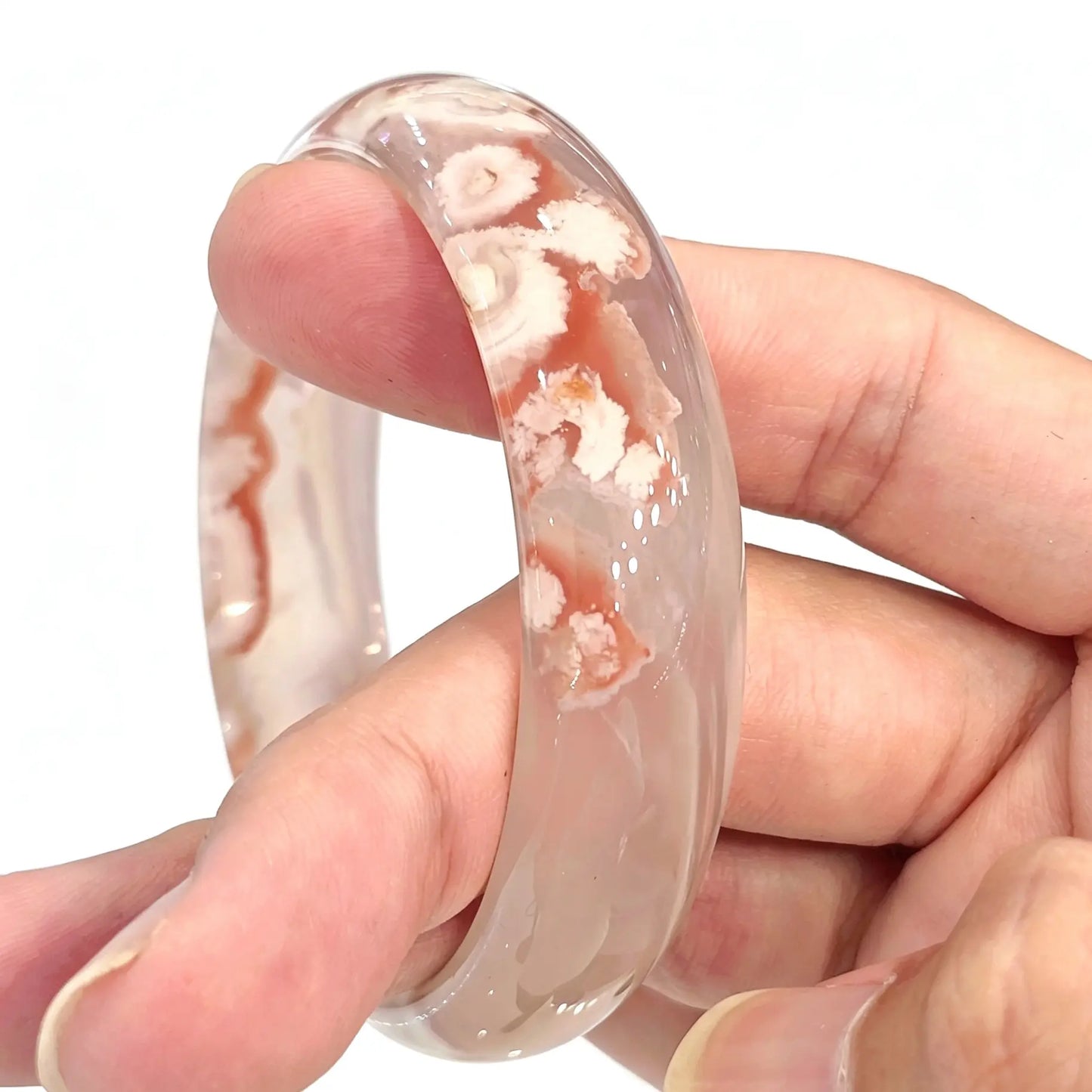Main view of cherry blossom agate bangle held between fingers showing translucent chalcedony matrix and grapefruit red blooms
