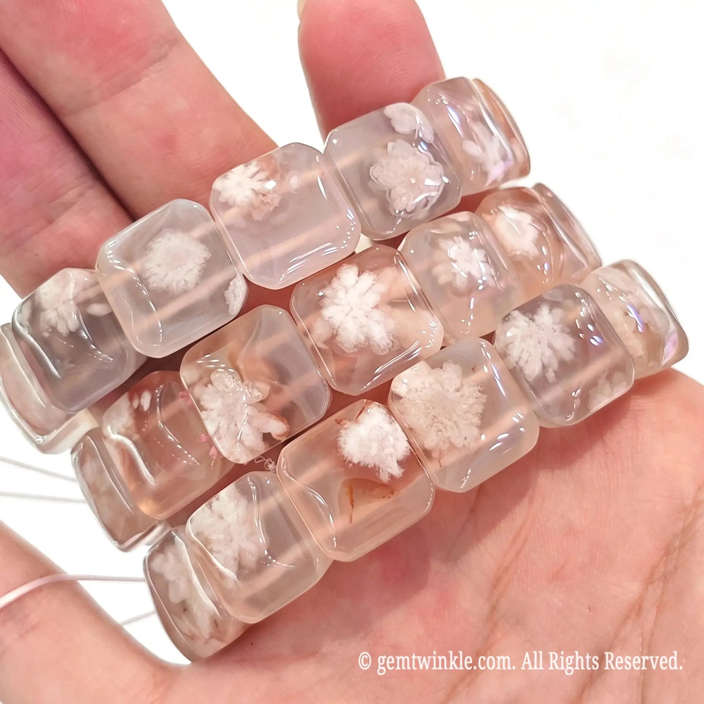 Close up handheld view of square cherry blossom agate beads showing white floral inclusions