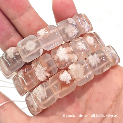 Close up handheld view of square cherry blossom agate beads showing white floral inclusions